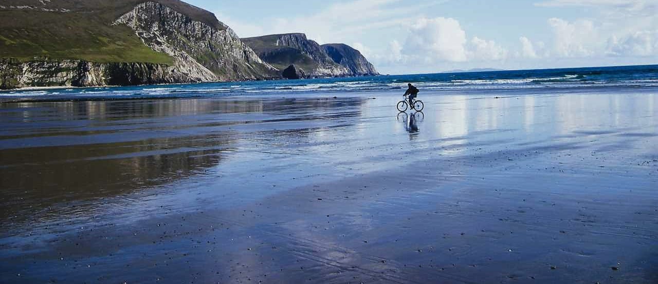 Achill island beach with a cyclist silhouette, sea and mountain in background