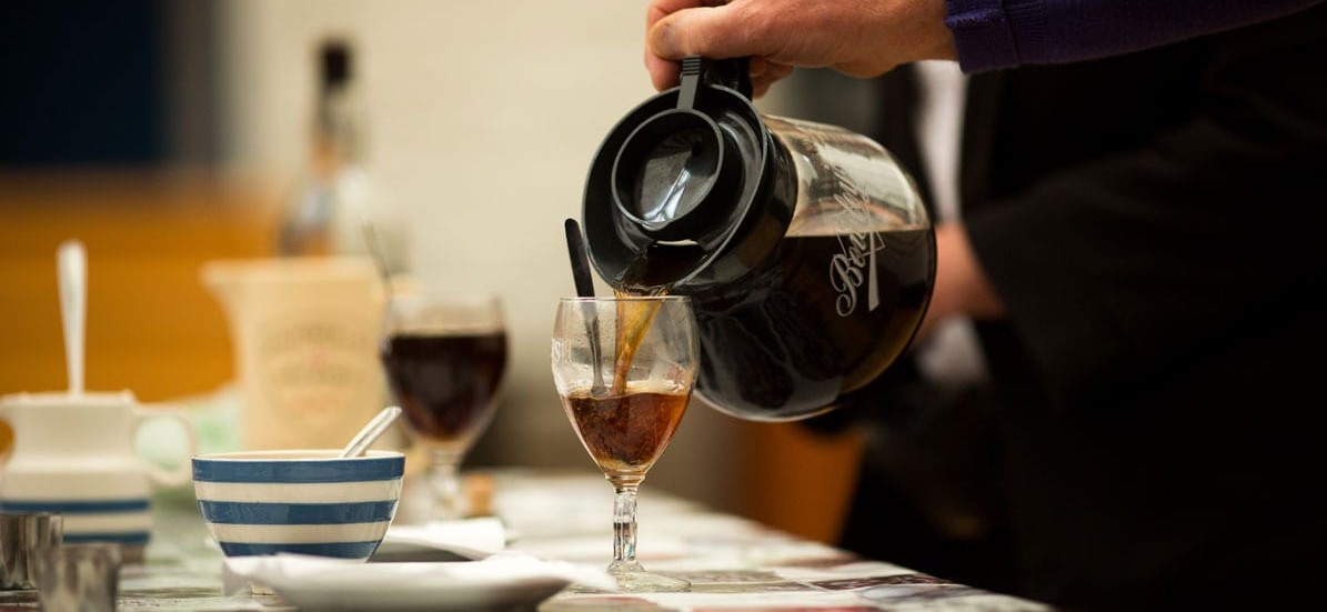 black coffee being poured into a glass of whiskey to make irish coffee