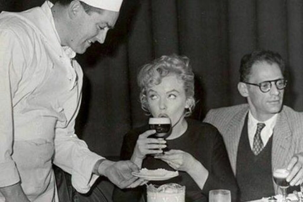 black and white photo of joe sheridan serving irish coffee to marilyn monroe, arthur miller sitting next to her