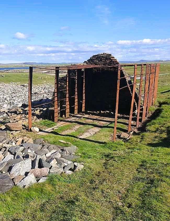 primitive house-like structure made of stone, supported by a metal structure to the front. Annagh Head on Mullet Peninsula