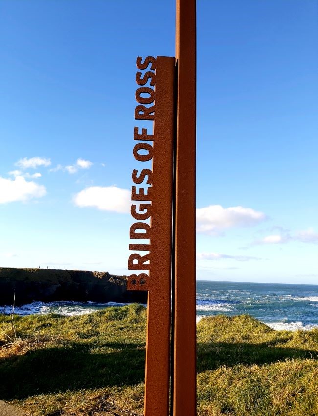 metal sign at the wild atlantic way with bridges of ross letters on the side, sea and cliffs in background