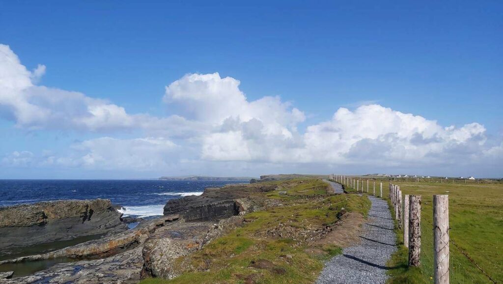 Cliff path at bridges of ross, wooden posts to the right marking out farmland, gravel path in the middle and sea on the left