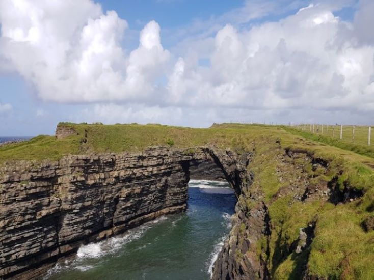 bridges of ross in county clare- rocky arch across the seapool, sky in background