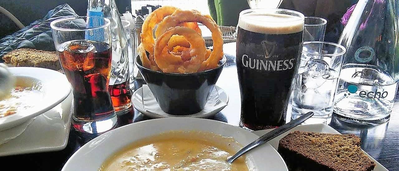 food and drink on the table - chowder soup, onion rings, pint of guinness, water, white wine