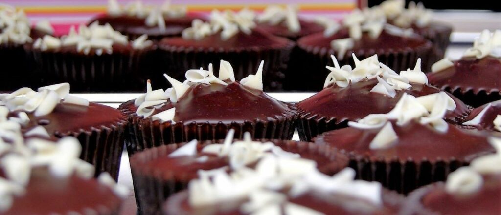 Close up of a cluster of chocolate muffins with dark chocolate genache and white chocolate shavings on top at a farmers market food festival