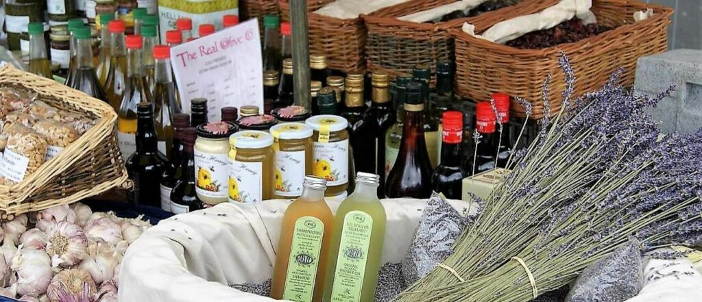 market at a food festivals stall with wicker basket with lavender, jars of jam, oils, garlic bulbs and dried hers, 