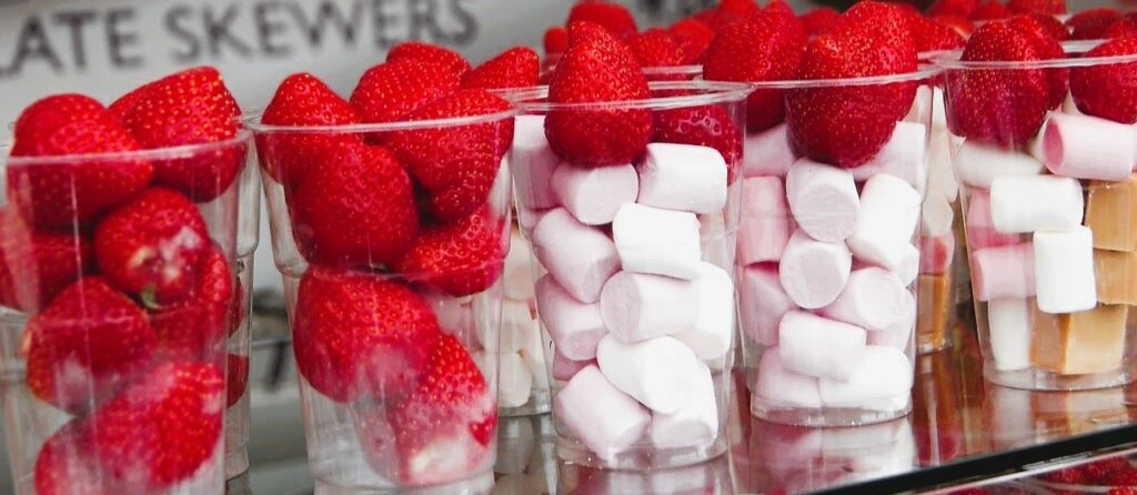 row of plastic cups filled with marshmallows and strawberries ready to have chocolate poured over at an outdoor stall for best time to visit ballina festival in July