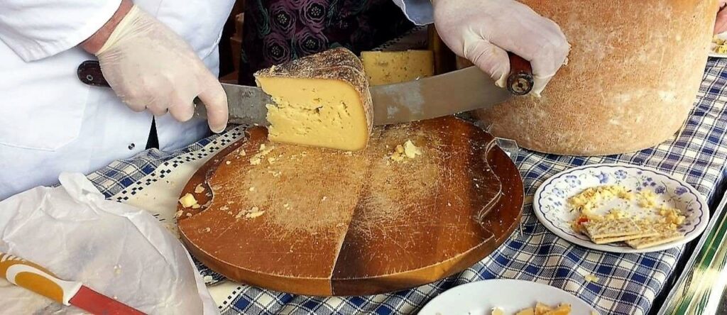 close up of a cheesemonger stall holder cutting up a wheel of cheese on a wooden block