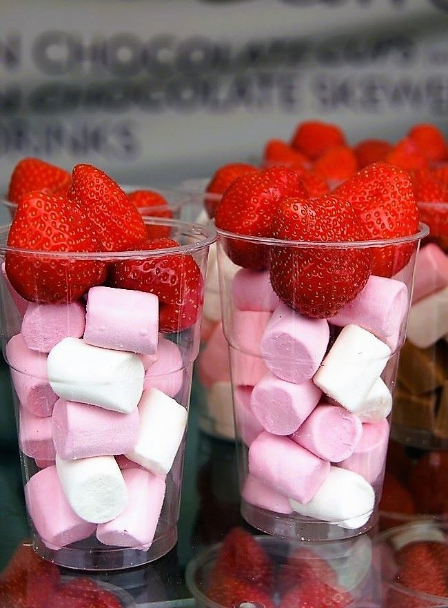 two see-through cups of marshmallows topped with strawberries ready for chocolate to be poured over the top, on a van counter