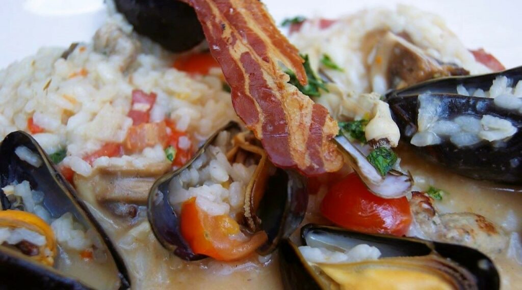 paella dish with rice, mussels in white wine sauce and crispy bacon at food festivals