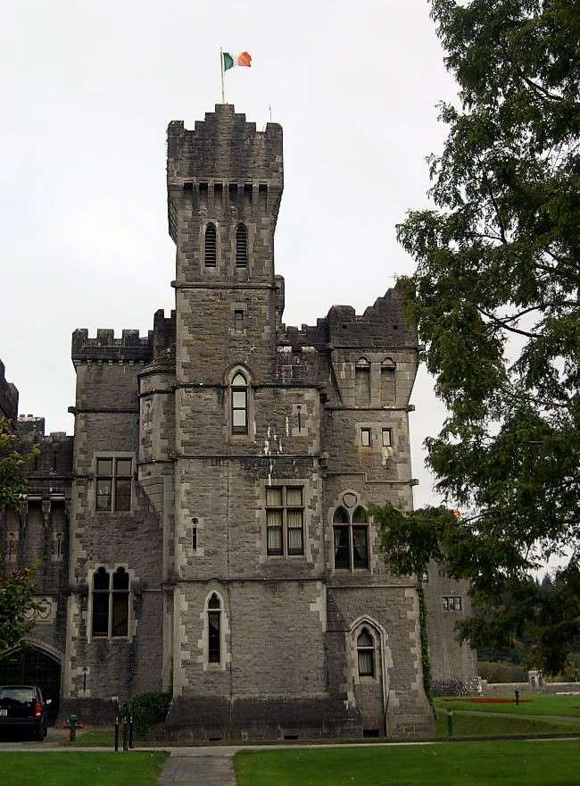 Ashford Castle - detail of a neogothic grey stone tower with ramparts, part of the castle, irish flag on top. Accommodation for a weekend in Cong. 