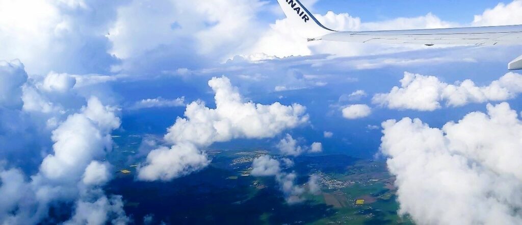 View from a plane window at blue sky, white clouds, the wing of a plane, how to travel to Ireland's West Coast