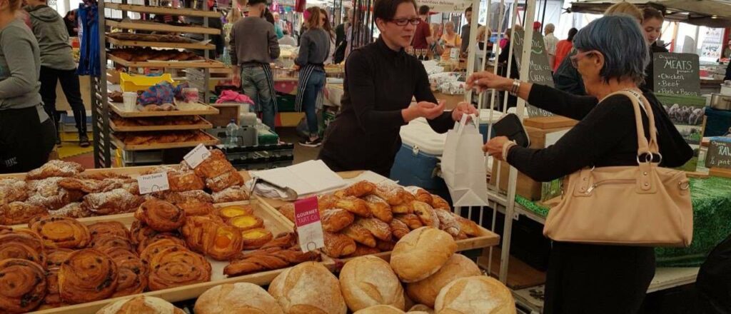 one of the things to do in Limerick is the milk market - market stall with breads and baguettes, seller handing a female shopper a bag with bread bought