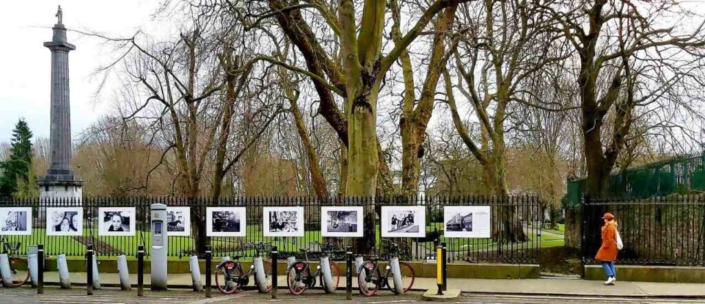 things to do in limerick - view of the railings on people's park with photo exhibition on them. bike rack with bikes in front, greenery and trees behind railings. 