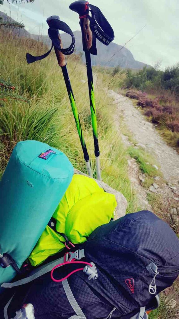 Hiking backpack and sleeping bag with hiking poles by the side of a walking path on the West Highland Way