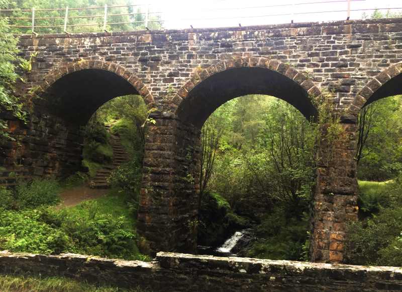 Stone arch railway bridge across a forest river with a hiking path underneath it