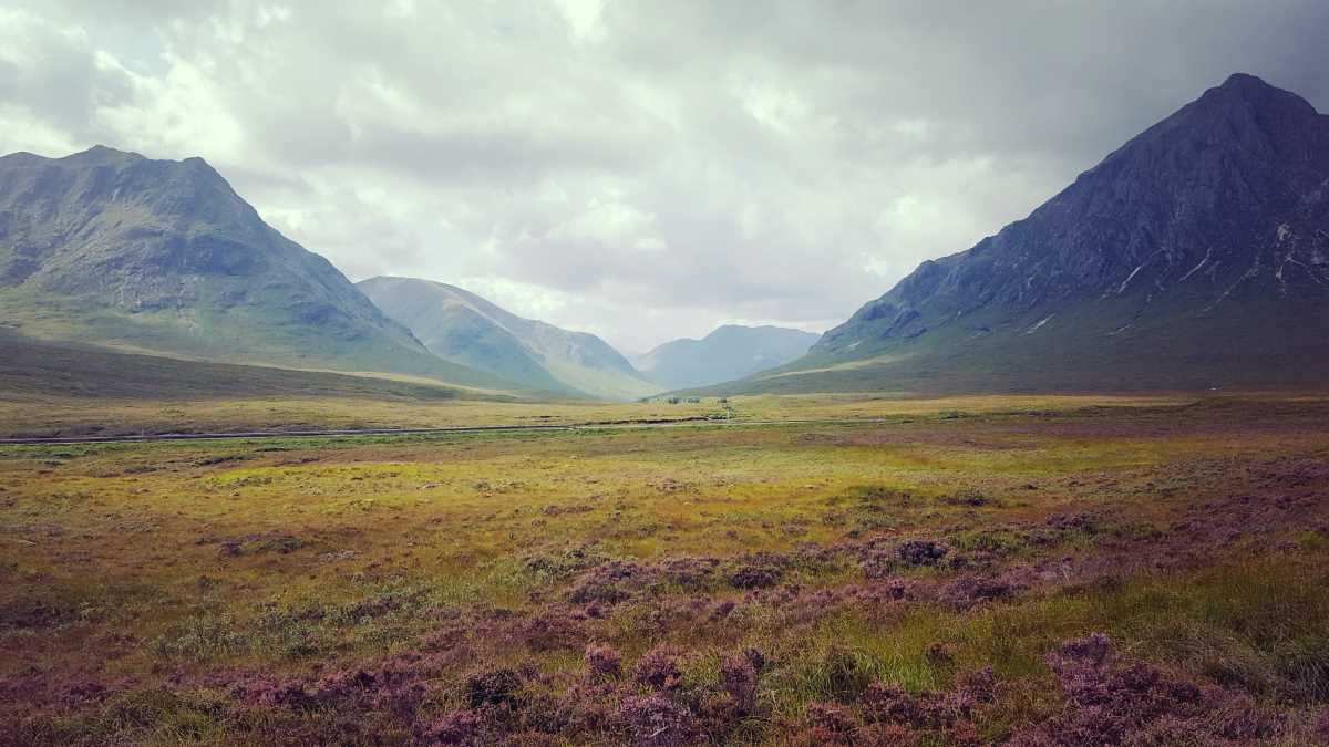 View of a mountain pass along the West Highland Way in Scotland, moor in foreground, hills with clouds in the background.