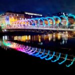 Milllenium Bridge in Dublin on a dark January evening, lit up in rainbow colours, reflecting int he Liffey