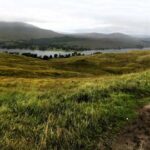 Scottish Highlands scenery with green marshy land, country road and hills rising in the distance with mist.