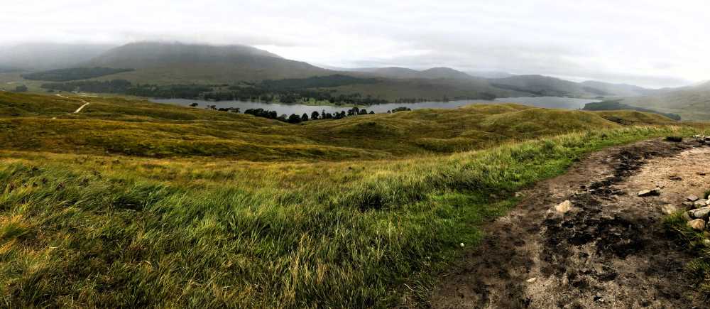 Scottish Highlands scenery with green marshy land, country road and hills rising in the distance with mist.